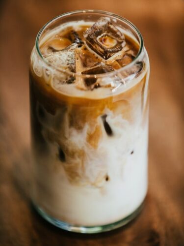 Glass with coffee, milk, and ice on wooden table