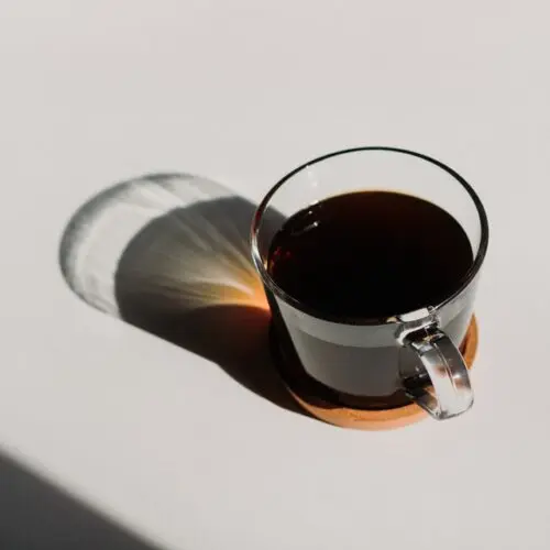 cup of black coffee in clear glass mug with sun reflecting through on white surface, how decaf coffee is made