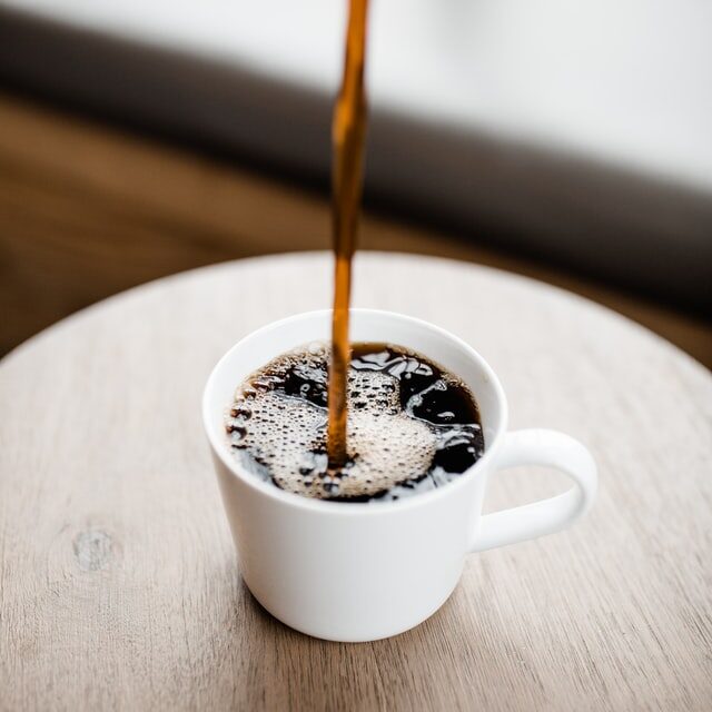 The Best Coffee Makers For Under 50 Bucks In 2026 2 stream of coffee pouring straight down into a white mug on a wooden table