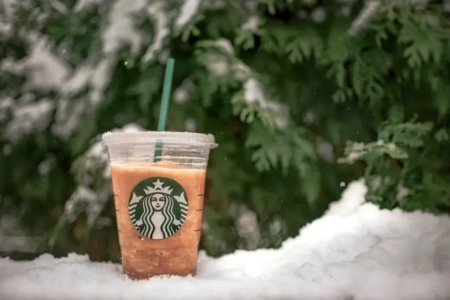 Starbucks iced coffee sitting in snow with snowy spruce tree in background