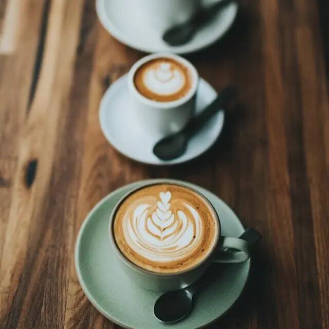 two espresso beverages on saucers with spoons on wood table
