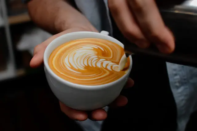 barista pouring milk into flat white to create artful design
