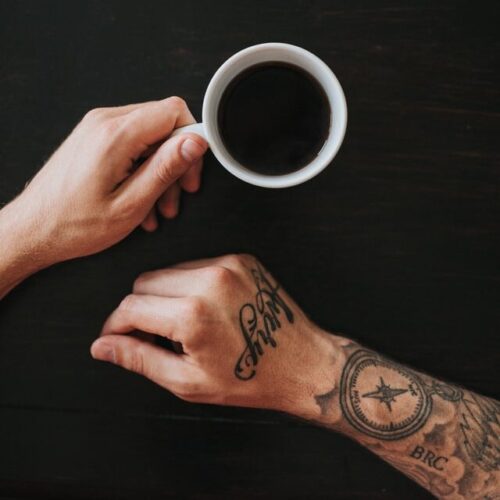 tattooed arms holding mug of black coffee black surface, ratio of coffee to water, coffee water ratio