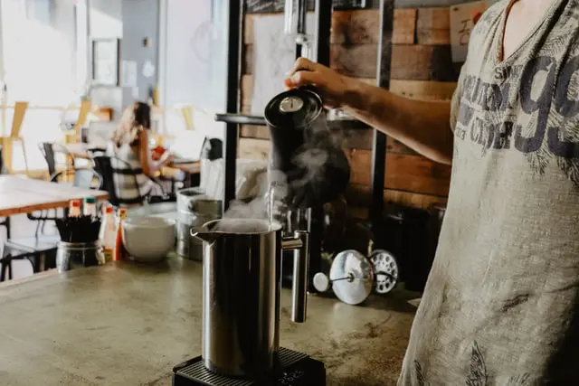 How To Use French Press Coffee Makers + The #1 Mistake 5 barista pouring water from kettle into stainless steel French press