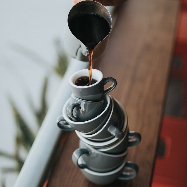 Coffee pouring into a stack of mugs