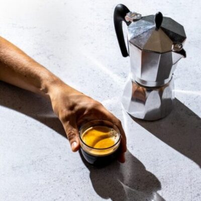 espresso shot in hand beside Moka pot, coffee for Moka pot