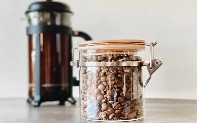 Best Coffee Grinder For French Press: Our 2026 Picks 1 glass jar of coffee beans with french press in the background, best coffee grinder for french press