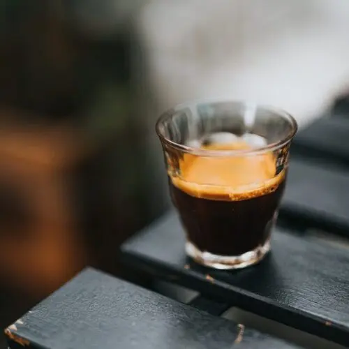 How Much Caffeine is in a Shot of Espresso? +5 Proven Facts 4 espresso shot in glass on edge of black outdoor table